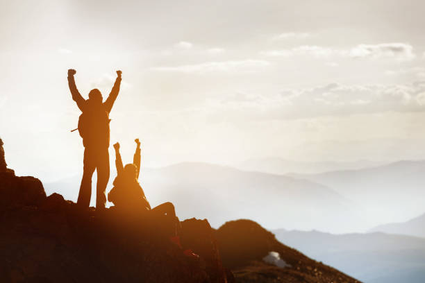 istock Two happy silhouettes tourists at mountain top success win 1069684594