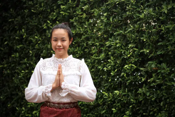 Asian girl wearing typical,traditional Thai dress with identity Thai culture Sawasdee,Welcome expression on trees background