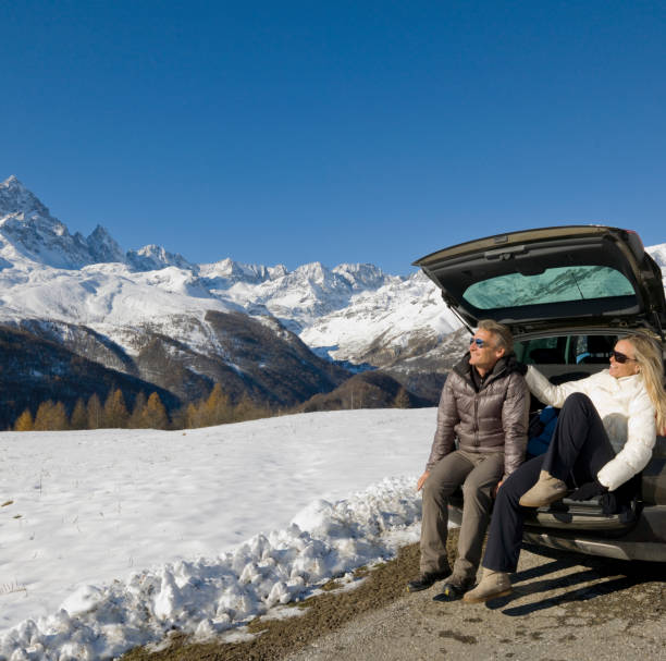 Couple sit on car tailgate, on mountain road