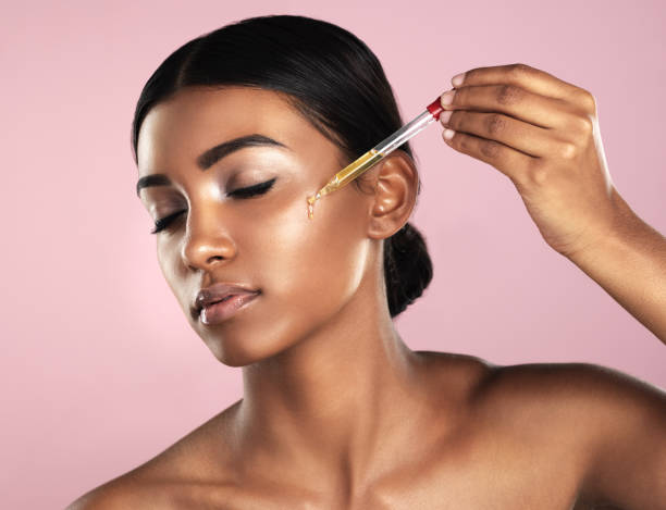 Her skin will be the envy of all Studio shot of a beautiful young woman applying essential oil to her face with a dropper posing against a pink background face serum stock pictures, royalty-free photos & images