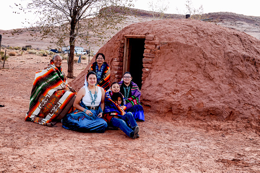 A happy multi-generational family of Native American Navajo people sitting happily outside their traditional Hogan