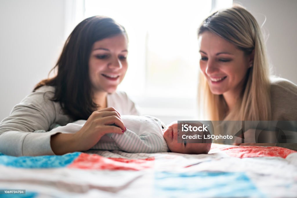 Two friend girl with a newborn baby on bed The Two friend girl with a newborn baby on bed Two People Stock Photo