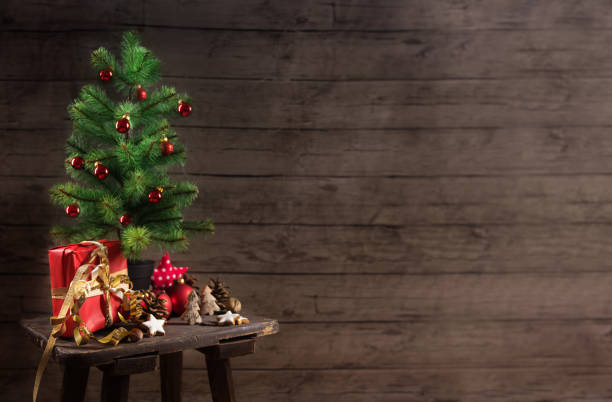 istock artificial christmas tree with red baubles, gift box and decoration on an small table in front of a rustic wooden wall, generous copy space 1069735132