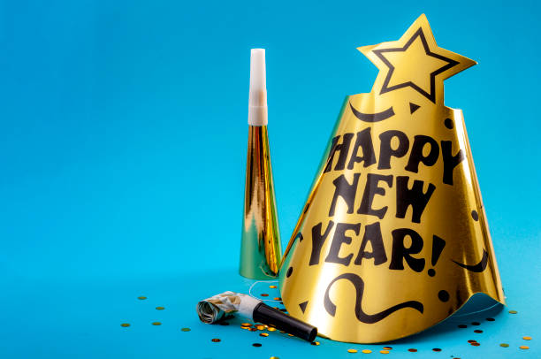 happy new year concept with a festive hat, noisemakers, confetti, party blower  and paper trumpet isolated on blue background with copyspace - wind instrument imagens e fotografias de stock