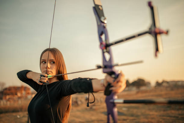 Teenage girl on archery training at sunset One teenage girl practicing archery outdoors at sunset on the field. bow and arrow photos stock pictures, royalty-free photos & images