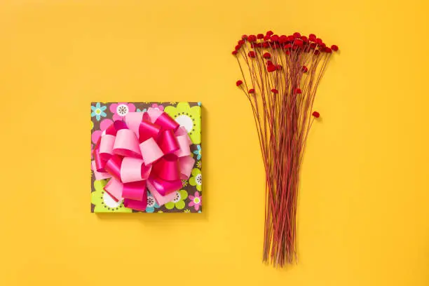 Bright gift box and a bouquet of dried red flowers on yellow background.