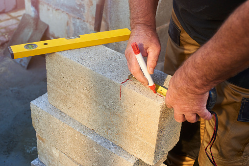 Building contractor measuring concrete block with tape measure and marking on guidelines to make his cuts with a marker pen