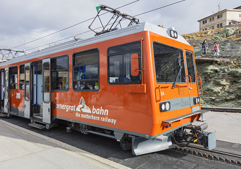 Mt. Gornegrat, Switzerland - September 16, 2018: a Gornergrat Railway passenger train standing at the Gornergrat station on the top of the mountain, people in the background. The Gornergrat Railway (German: Gornergrat Bahn, abbreviated as GGB) is a mountain rack railway in the Swiss canton of Wallis, connecting the town of Zermatt with the summit of the Gornergrat. The Gornergrat (English: Gorner Ridge) is a rocky ridge overlooking the Gorner Glacier south-east of Zermatt in Switzerland.