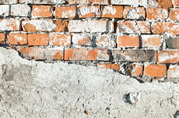 old weathered brick wall partially covered with falling off concrete-background image