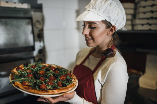 istock Female pizza maker holding pizza margharita in the restaurant kitchen 1069790838