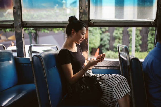 mensajes de texto de mujer joven en un teléfono móvil en un autobús público en bangkok, tailandia - bangkok mass transit system fotografías e imágenes de stock