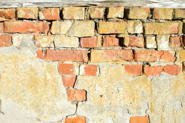 old weathered brick wall partially covered with falling off concrete-background image