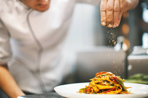 Sprinkling seasonings from high up. Unrecognizable male chef sprinkling spices on a dish in a commercial kitchen. fine dining stock pictures, royalty-free photos & images