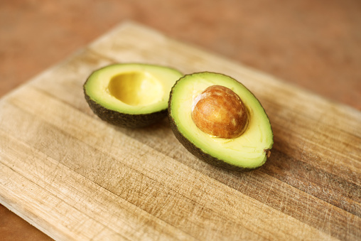 Two halves of a sliced avocado resting on a wooden cutting board
