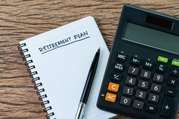 Retirement planning concept, calculator with empty notepad with pen and handwriting underline headline as Retirement Plan on wood table, plan of saving and investment for expense after retire life.