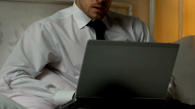 Man typing weekly report on laptop pc, busy journalist working on article in bed