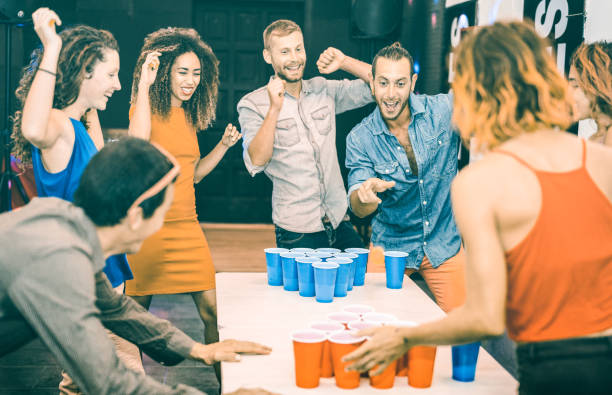 amigos felizes jogando cerveja pong na juventude jovens de - conceito de viagens e alegria com mochileiros ter desligado a diversão no guesthouse - albergue em atitude genuína lúdico - verde-azulado e laranja filtro - time table - fotografias e filmes do acervo