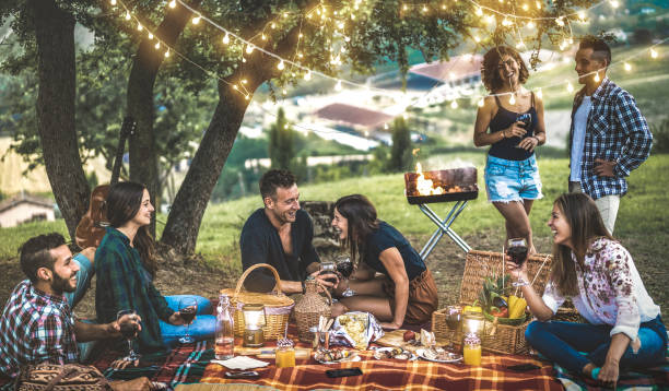 amici felici che si divertono in vigna dopo il tramonto - giovani campeggio millenario al picnic all'aperto sotto le luci delle lampadine - concetto di amicizia giovanile con i giovani che bevono vino alla festa barbecue - light meal foto e immagini stock