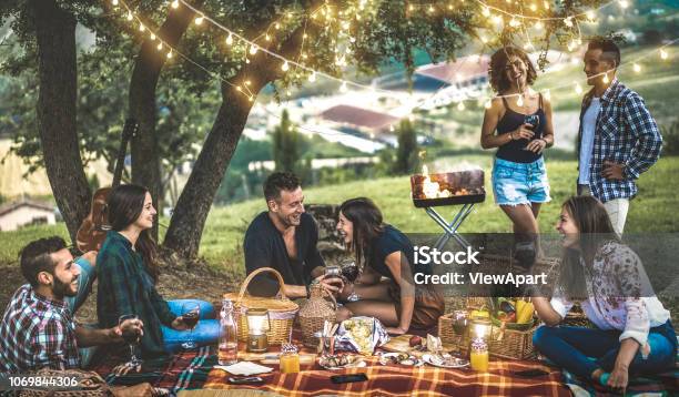 Happy Friends Having Fun At Vineyard After Sunset Young People Millennial Camping At Open Air Picnic Under Bulb Lights Youth Friendship Concept With Young People Drinking Wine At Barbecue Party Stock Photo - Download Image Now