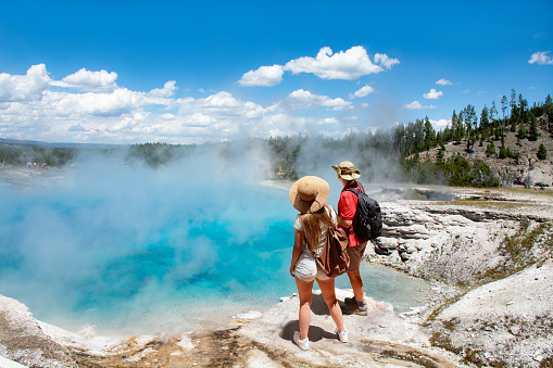 Couple relaxing and enjoying beautiful view of gazer on vacation hiking trip. Man and woman with backpacks looking at Excelsior Geyser from the Midway Basin in Yellowstone National Park. Wyoming, USA