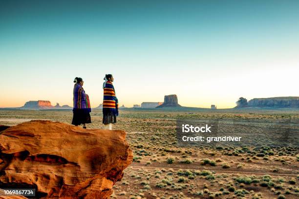 Two Traditional Navajo Native American Sisters In Monument Valley Tribal Park On A Rocky Butte Enjoying A Sunrise Or Sunset Stock Photo - Download Image Now