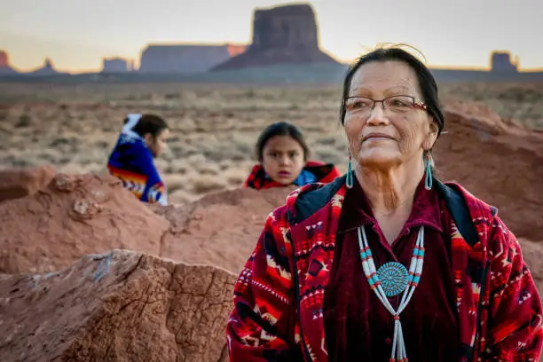 Beautiful proud portrait of a traditional Navajo grandmother with her grandson and granddaughter in front of the famous rock formations of the Monument Valley Tribal Park in Northern Arizona