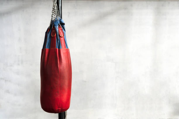 istock Red punching bag is hanging on cement wall in boxing gym. 1069881024