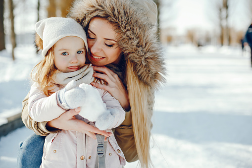 A young and stylish mom plays with her little beautiful daughter in a snowy snowy park