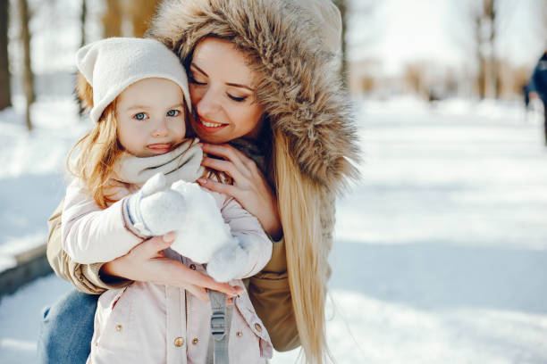 mother with daughter A young and stylish mom plays with her little beautiful daughter in a snowy snowy park kids winter coat stock pictures, royalty-free photos & images