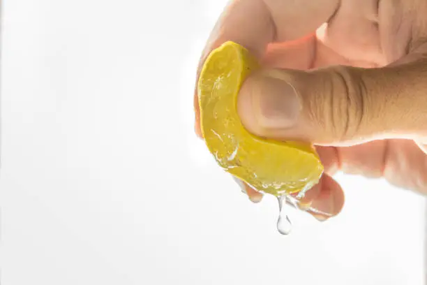 close up Human hand squeezing half of lemon on white background