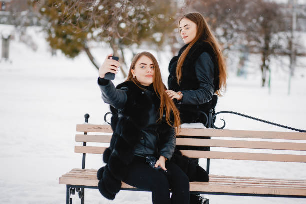 Cute girls sitting in a winter park. Sisters use the phone