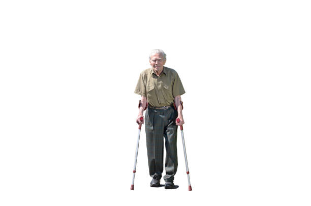 Senior retired man walking on crutches on a walkway between green hedges in a residential suburb approaching the camera front on