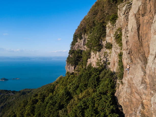Mid adult Japanese man rock climbing in an extremely high cliff location op a huge rock face