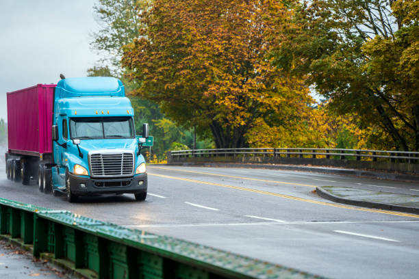 istock Big rig day cab semi truck transporting container on flat bed semi trailer driving on the wet road in rain autumn weather 1069911018