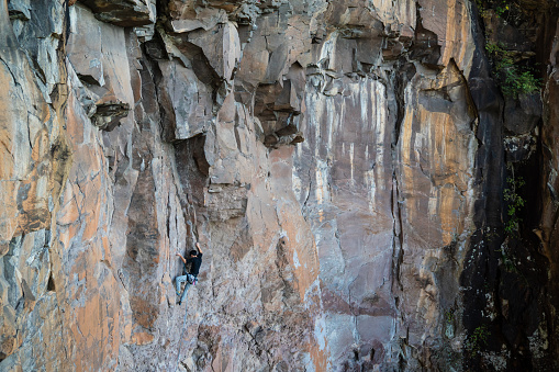 Mid adult Japanese man rock climbing in an extremely high cliff location op a huge rock face