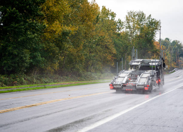 Empty big rig car hauler semi truck running on autumn rainy road Empty Big rig dark car hauler powerful semi truck going to loading cars on two levels semi trailer driving safety on the slippery wet road in rain with rain dust and autumn trees on the side shipping heavy equipment machinery stock pictures, royalty-free photos & images