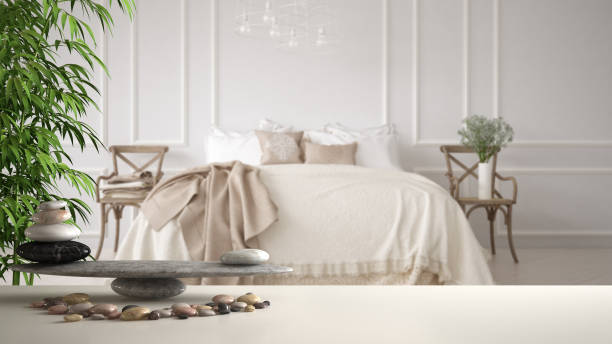 estante de la mesa blanca con guijarro equilibrio y bambú planta sobre vintage dormitorio con la cama repleta de almohadas y mantas, zen concepto interiorismo - feng fotografías e imágenes de stock