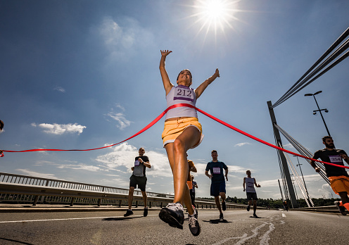 Low angle view of satisfied marathon runner celebrating her victory while crossing the finish line.