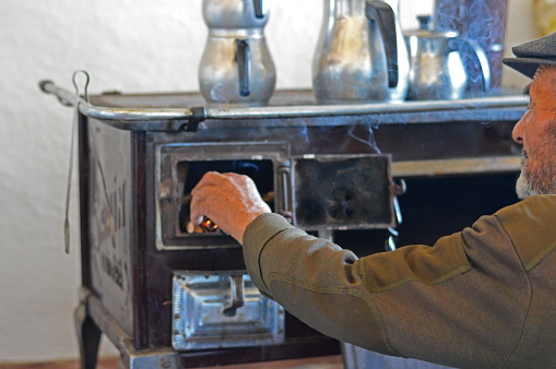 Senior Turkish Man Putting Logs In Fireplace who lives in a small country house