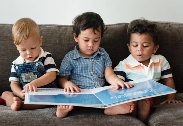 tres niños leyendo un libro sobre un sofá - child book reading baby fotografías e imágenes de stock