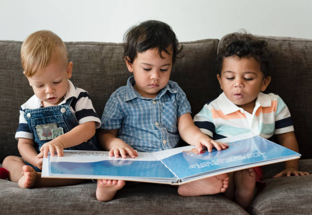 trois petits garçons, lecture d’un livre sur un canapé - baby book toddler reading photos et images de collection
