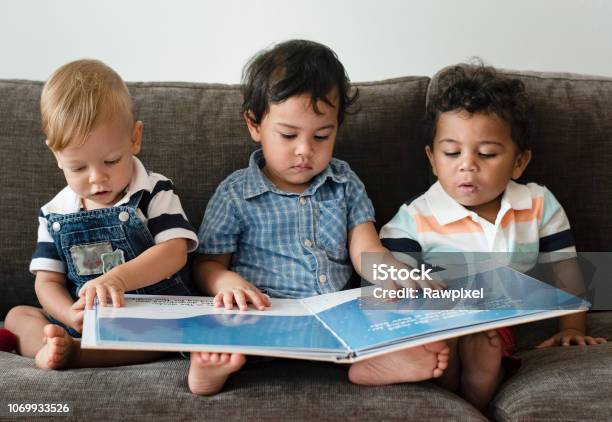 Three Little Boys Reading A Book On A Sofa Stock Photo - Download Image Now - Baby - Human Age, Reading, Toddler