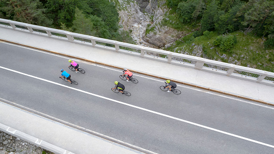 Five male and female riders riding road bikes on bridge.