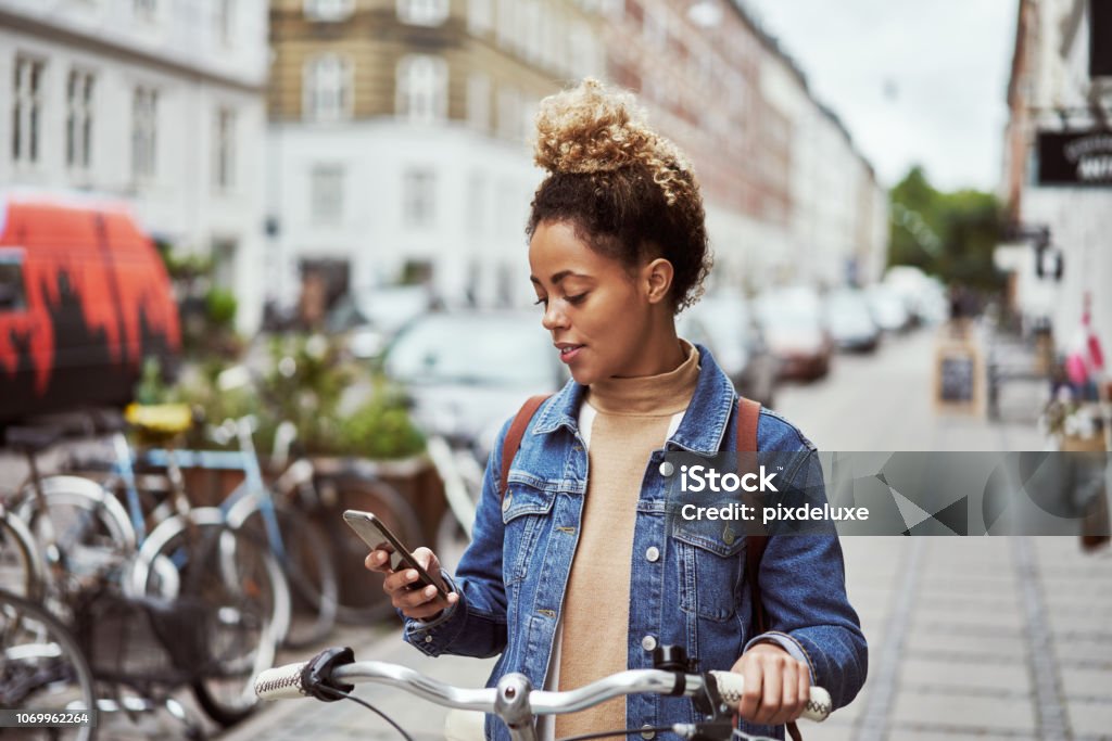 Looking for bike shops nearby Shot of an attractive young woman using her cellphone while out cycling through the city People Stock Photo