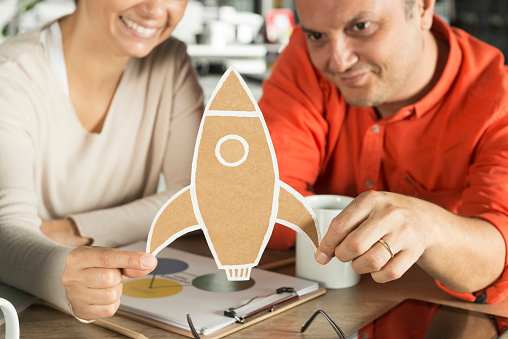 Two business person holding and looking toy rocket.