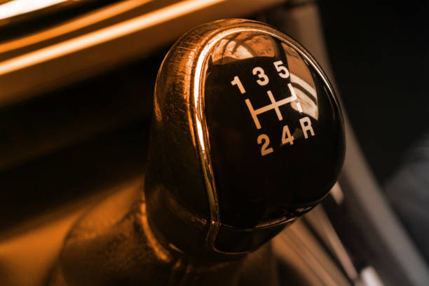 Macro shot of a manual gear shifter knob in a dark car interior, highlighting gear layout and metallic details.