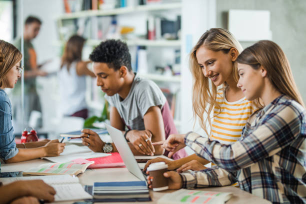 istock Happy female students e-learning with their friends in library. 1069968782