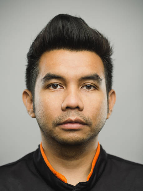 Real malaysian young man with blank expression Close up portrait of asian young man with blank expression against gray background. Vertical shot of real malaysian man staring in studio with black hair and quiff. Photography from a DSLR camera. Sharp focus on eyes. rockabilly hair men stock pictures, royalty-free photos & images