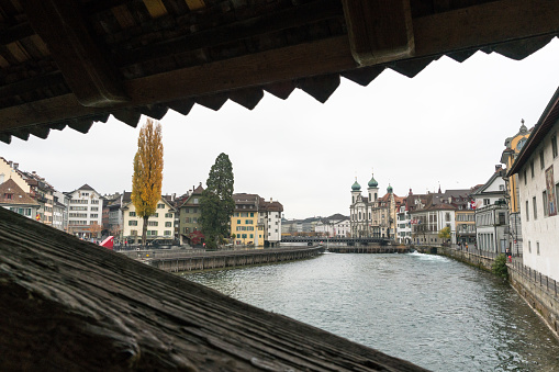 Lucerne, LU / Switzerland - November 9, 2018: the famous Swiss city of Lucerne cityscape skyline and Jesuit church with the river Reuss panorama view and the historic Rathaussteg with tourists in the foreground