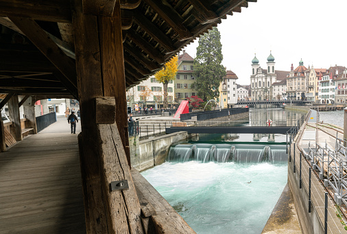 Lucerne, LU / Switzerland - November 9, 2018: the famous Swiss city of Lucerne cityscape skyline and Jesuit church with the river Reuss panorama view and the historic Rathaussteg with tourists in the foreground
